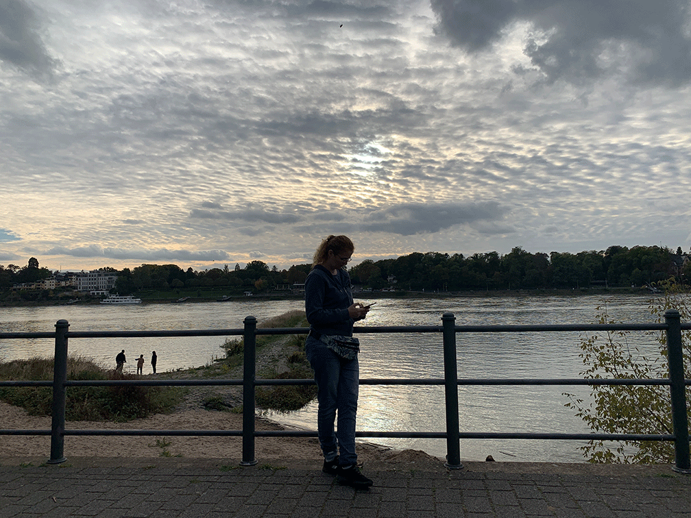 Frau mit Handy im Gegenlicht am Rhein