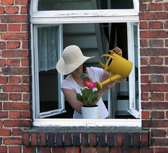 Frau am Fenster gießt Blumen